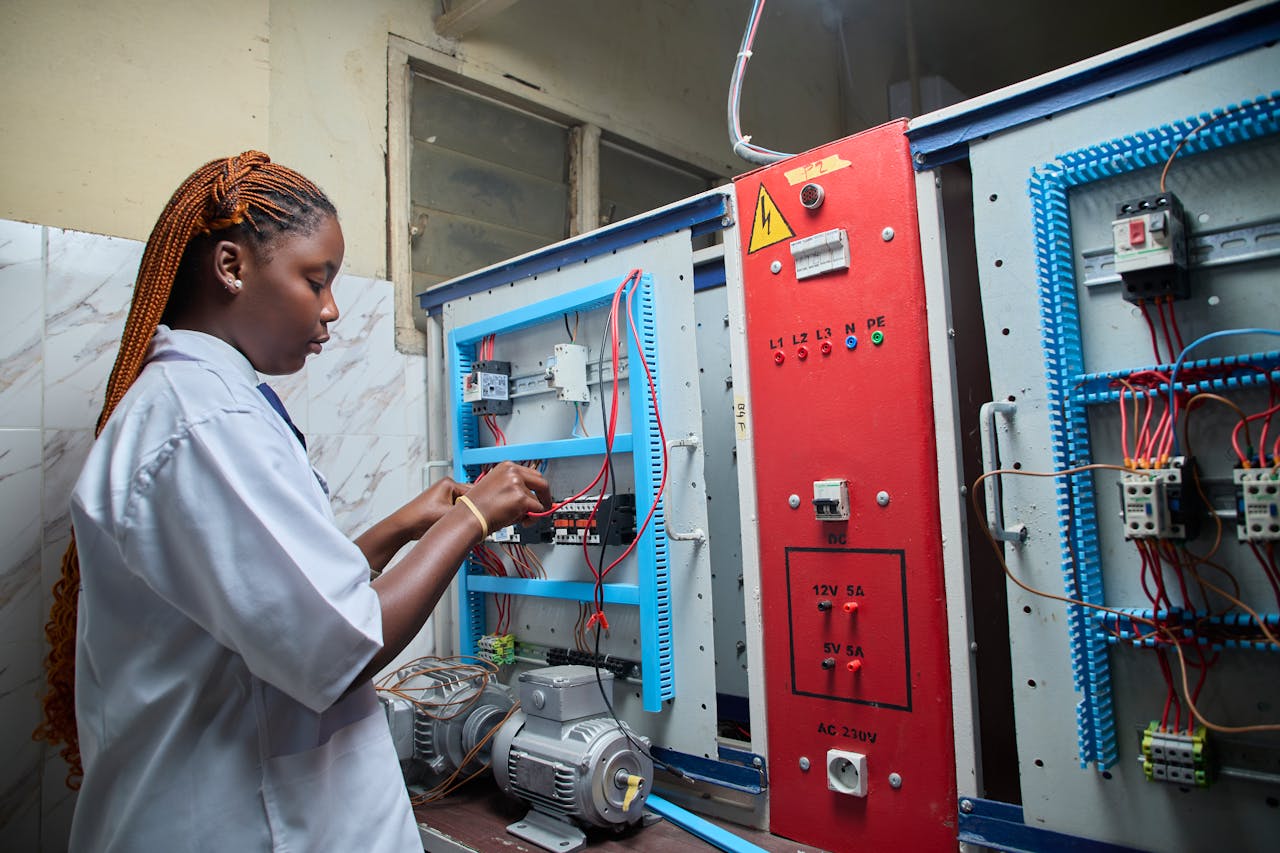 Young female technician repairing electrical control panel in industrial setting.